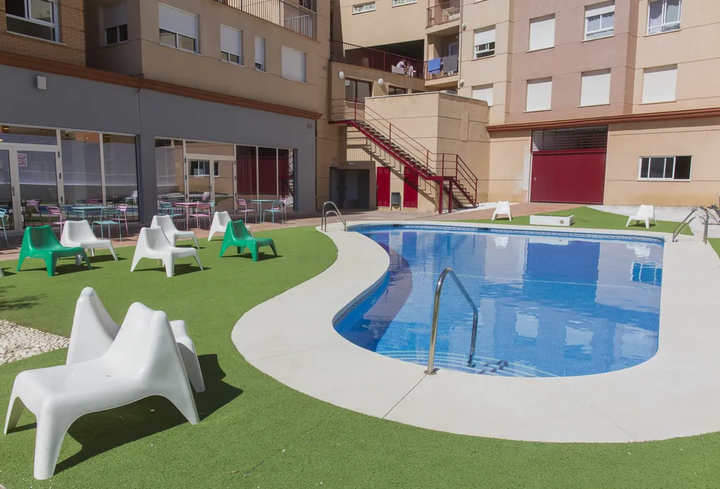 Piscina del patio de la residencia rodeada de césped y tumbonas blancas