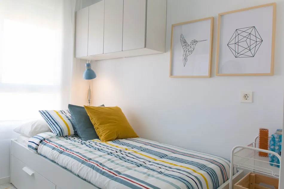 Habitación renovada de la residencia con cama a rayas, cojín amarillo y flexo azul