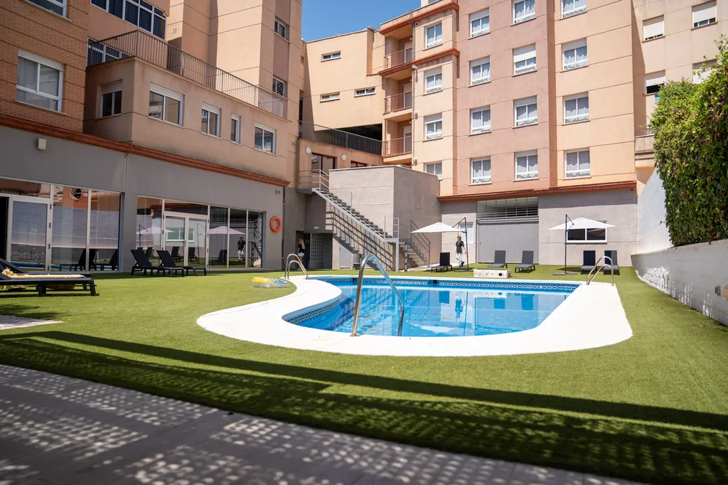 Piscina de la RUT rodeada de césped y hamacas en el patio