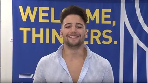 Diego sonríe ante el fondo azul «Welcome, Thinkers» de la RUT. Pulsa para ver su testimonio