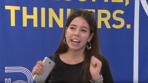 María habla con el móvil en la mano ante el fondo «Welcome, Thinkers». Pulsa para ver su testimonio