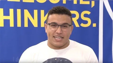 Nicolás, con gafas y camiseta blanca, ante el fondo azul de la RUT. Pulsa para ver su testimonio